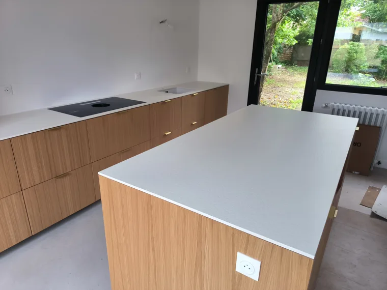 Cuisine avec îlot, façades en bois et plans de travail clairs.