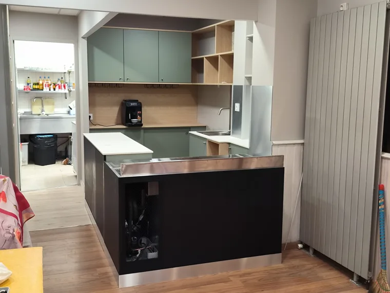Cuisine avec rangements verts, niches en bois et retour de plan de travail.