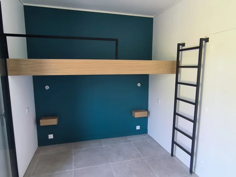 Mezzanine en bois avec échelle noire dans une pièce aux murs bleus.