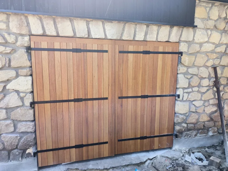 Double porte extérieure en bois, avec ferrures noires, dans un mur en pierre.