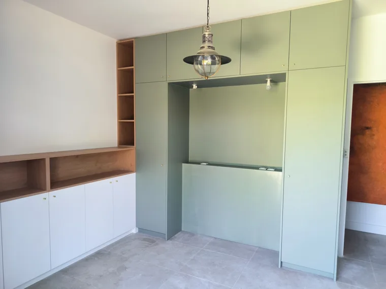 Meubles intégrés avec façades vertes, niches ouvertes et rangements bas.